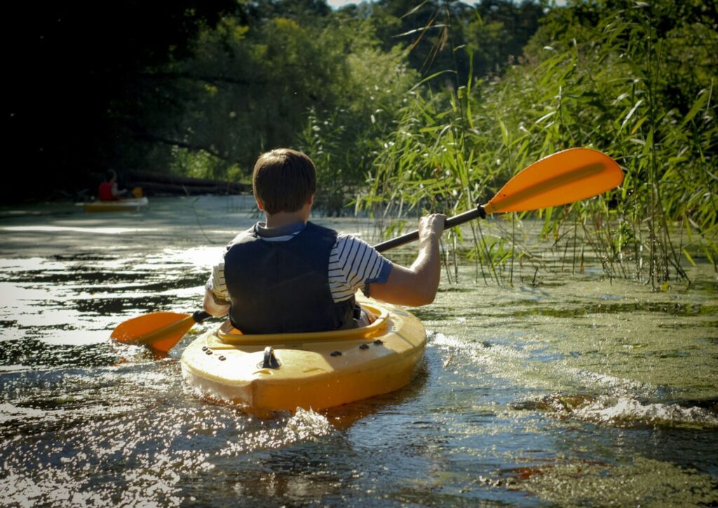 Guy in kayak floats on river, rearview